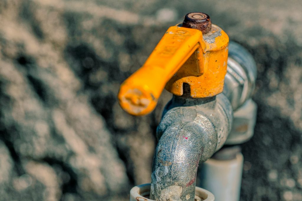 Close-up of an outdoor metal faucet with a yellow handle.